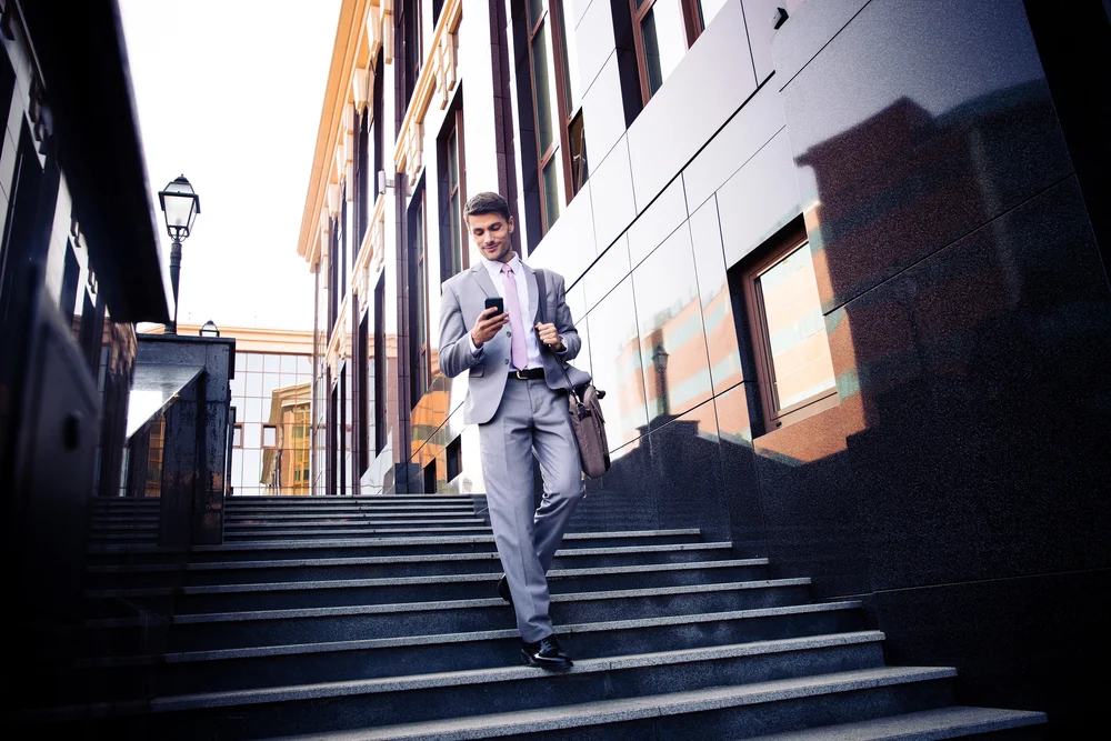 businessman walks down city steps while looking at his smartphone